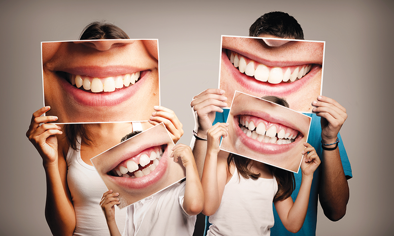 Family holding photos of smiling healthy teeth