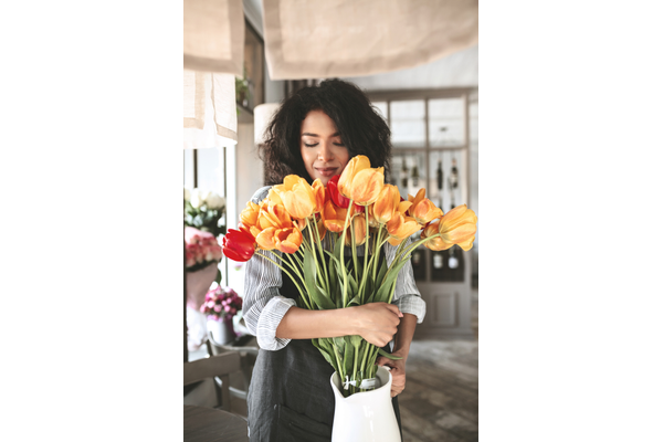 portrait of lady with dark curly hair holding a white vase with orange and red tulips