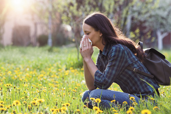 Allergy sufferer blowing nose outside experiencing more symptoms from climate change