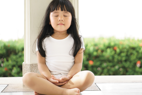 Calm kid sitting down cross-legged in meditation pose practicing mindfulness