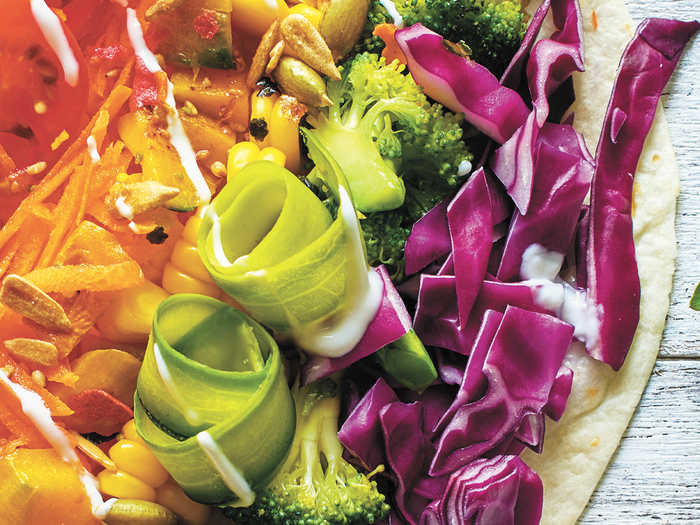 Tomatoes shredded carrots corn zucchini broccoli red cabbage on tortilla representing colorful vegetables