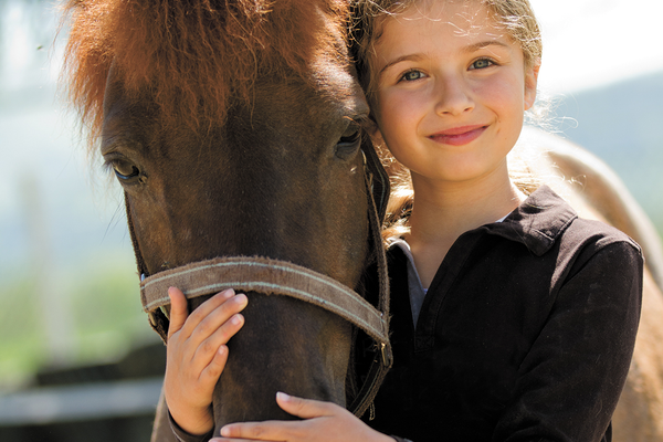 Kid smiling standing next to brown horse with reigns on embracing head