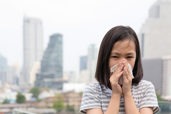 Child blowing nose into tissue in city from irritation of polluted air