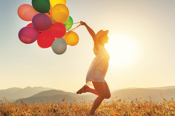Person running through field holding colorful balloons with mountains in background