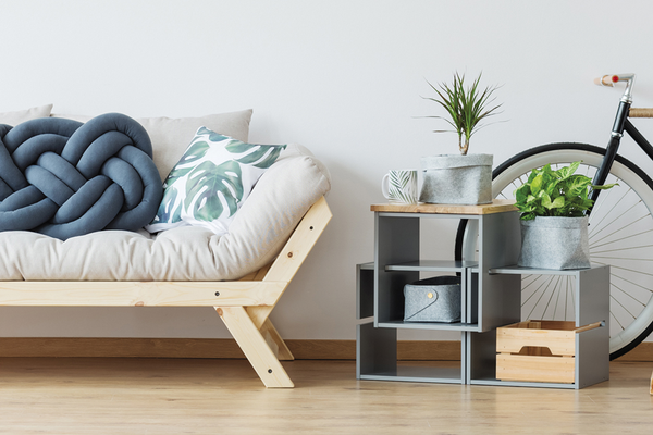 Simple, minimal living room with couch, throw pillows, end tables with plants and storage and bicycle