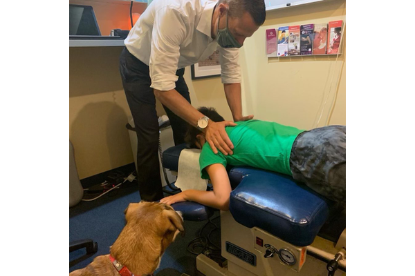 A child getting a chiropractic adjustment while his dog waits beside him.