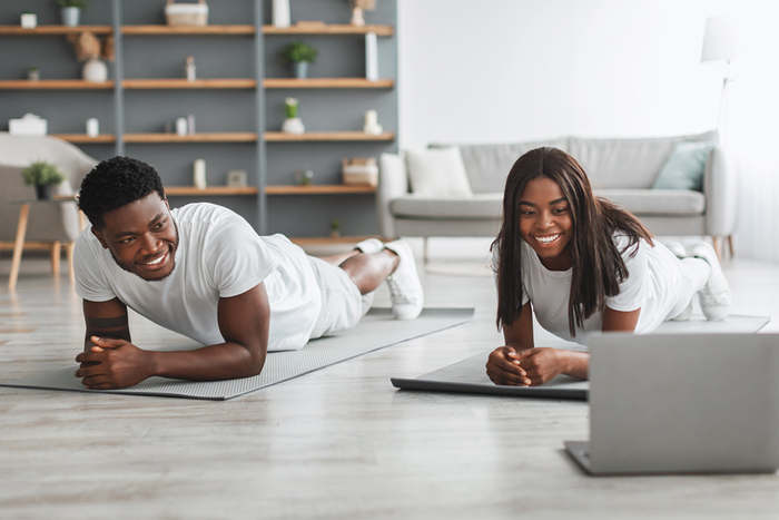 Two people planking on yoga mats while watching virtual workout on laptop