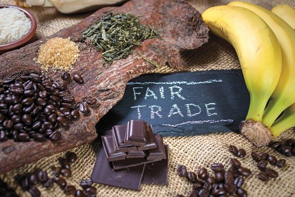 Bananas, chocolate bars, coffee beans, herbs, spices next to chalkboard sign reading Fair Trade