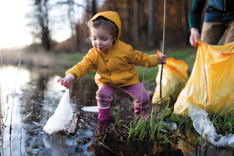 Child in rain gear standing in water picking up trash with parent