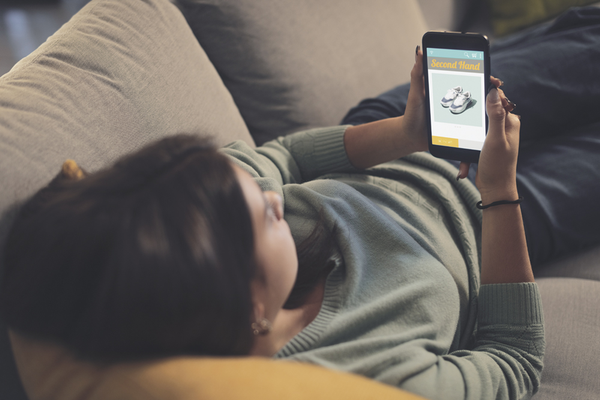 Person lying on couch shopping second hand items online through phone