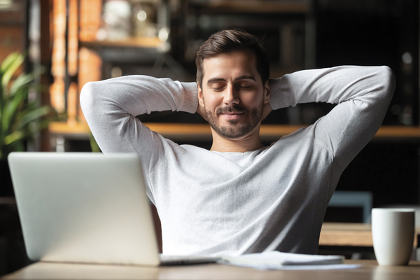 Person sitting at desk in front of laptop with arms stretched behind head in a relax position