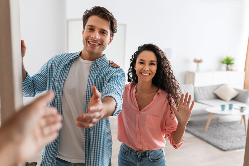 Couple opening door to greet guest with hand reaching out