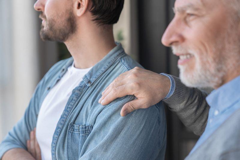 Father putting hand on son's shoulder, who has arms crossed and is looking in other direction