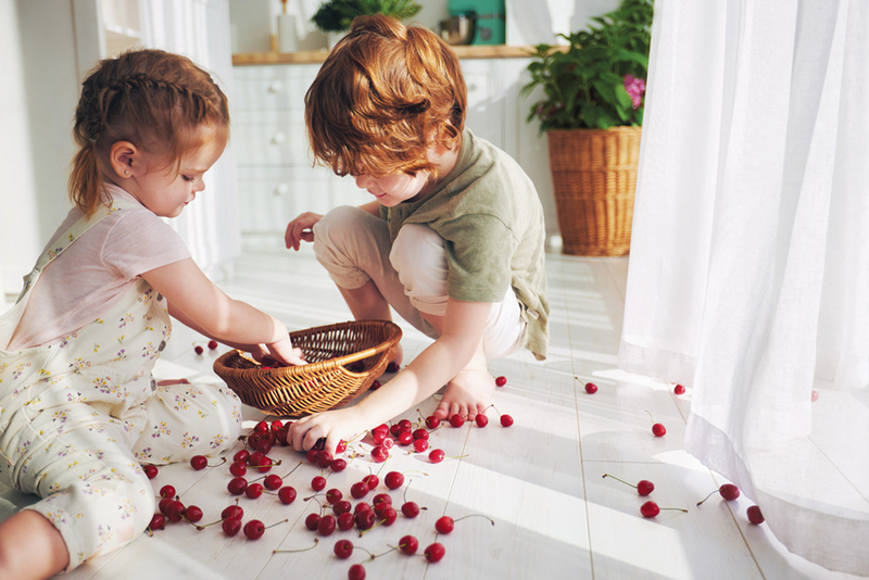Two kids on floor putting cherries in a wicker bowl