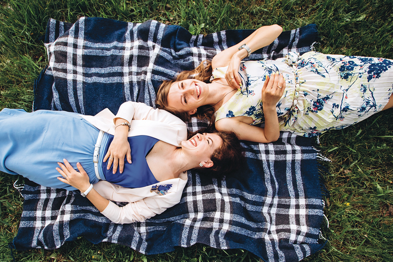 Two people lying on their backs on a plaid blanket on the grass
