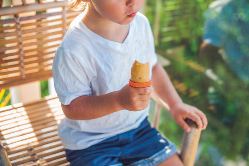 Child sitting on chair outdoors holding frozen orange treat
