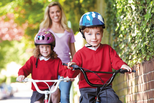Kids bicycling wearing helmets with mother walking behind them