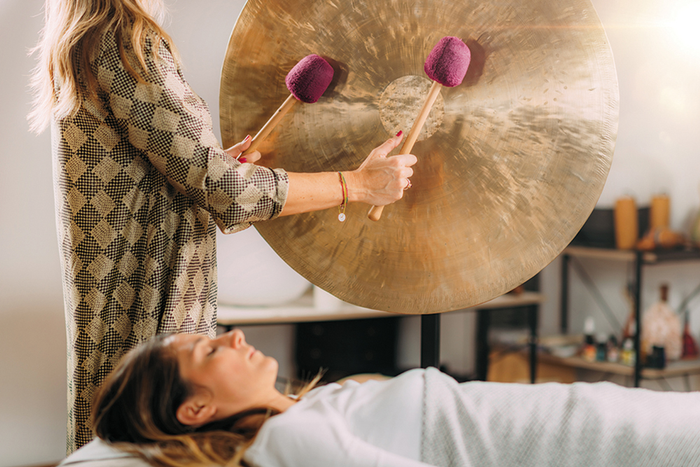 Person lying on table listening to practitioner using mallets to play sound healing gong