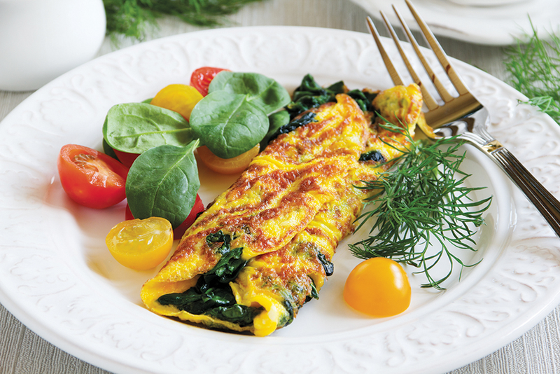 Spinach and artichoke omelette on plate with sliced tomatoes, fresh greens and fork